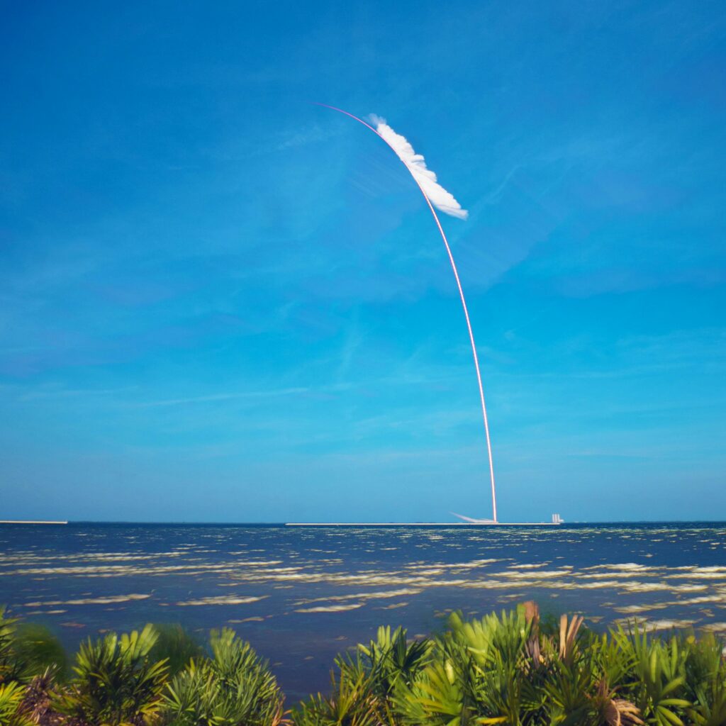 Captivating rocket launch leaving a trail over the ocean beneath a clear blue sky.